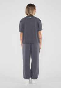 Top grigio a maniche corte con una vestibilità comoda e scollo rotondo, abbinato a pantaloni larghi coordinati. Presenta una marcatura minimale sul retro.