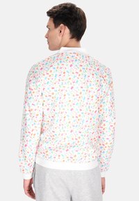 Witte sweatshirt met een kleurrijk sterrenpatroon in roze, blauw, oranje en groen, met een geribde zoom en boorden, gezien van de achterkant.