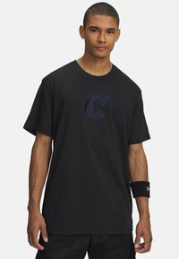 Sort bomulds t-shirt med et blåt broderet bogstav "C" på forsiden. Korte ærmer, rund halsudskæring og løs pasform.