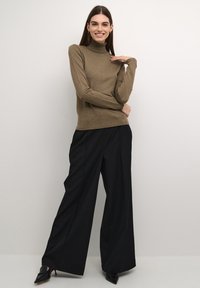 Beige garbónyakú pulóver hosszú ujjakkal, fekete széles szárú nadrággal és hegyes fekete magassarkú cipővel párosítva. Simács textura, testhezálló dizájn.