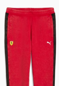 Røde sweatpants med sorte side-striber, elastisk talje, prydet med et gult Ferrari-logo og et hvidt Puma-logo nederst til venstre. Blød tekstur.