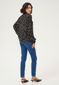Schwarze Bluse mit cremefarbenem abstraktem Muster, lange Ärmel mit gerafften Manschetten, kombiniert mit blauen geraden Jeans und schwarzen mules mit Absatz.