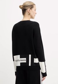 Maglione nero con una vestibilità rilassata, caratterizzato da un bordo bianco a contrasto all'orlo con dettagli del logo. Tessuto a maglia, maniche lunghe.