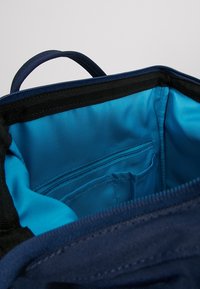 Vnitřek námořnické tašky s hladkým modrým podšívkou, malou zipovou kapsou a texturovaným černým lemem podél horního okraje.