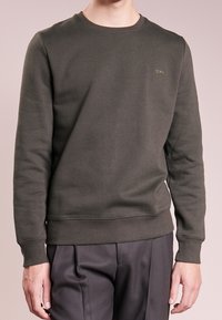 Sudadera verde oscuro hecha de un tejido suave, con un cuello redondo, puños y dobladillo acanalados, y un sutil logotipo en el pecho.