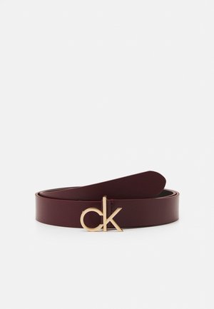 Ceinture en cuir marron foncé enroulée avec boucle dorée au logo "ck" placée devant sur fond blanc.