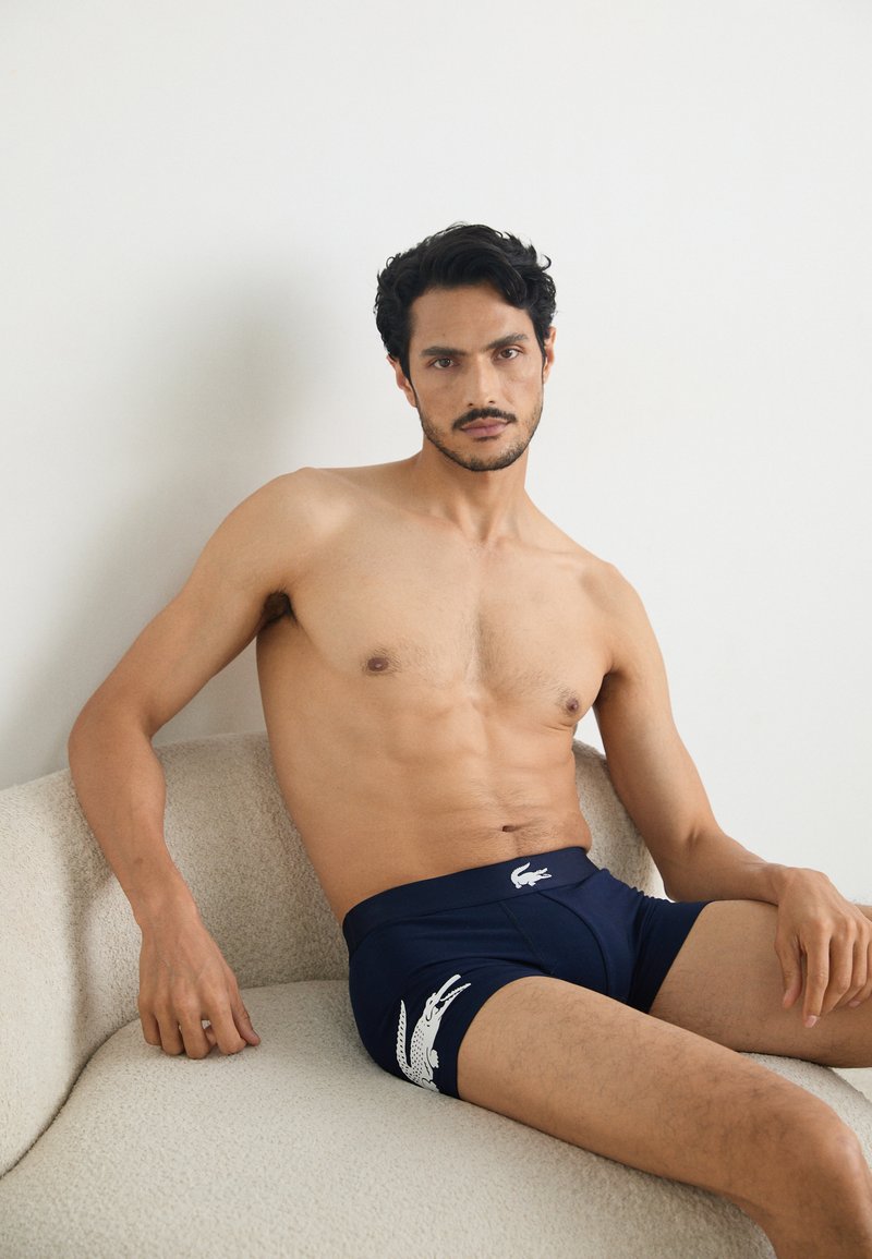 Marineblauwe boxershorts van rekbaar materiaal, met een wit Lacoste-logo op de onderste linkerzijde. Gladde textuur en aansluitende pasvorm.