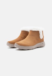 Beige Wildleder-Ankle-Boots mit einem weißen Kunstpelzkragen, die eine weiche Textur und eine flexible graue Gummisohle aufweisen. Lässiges Design für hohen Komfort.