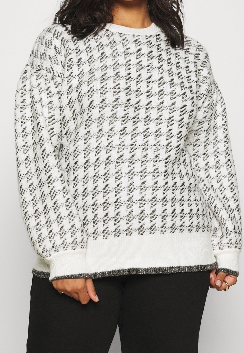 Femme portant un pull en tricot à motif pied-de-poule noir et blanc avec des poignets et un ourlet côtelés, associé à un pantalon noir.