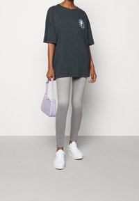 Camiseta negra oversize con un gráfico púrpura, jeans skiny grises, zapatillas blancas y un bolso texturizado de color púrpura claro.