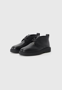 Zwarte leren schoenen met ronde neuzen, gestructureerde zwarte rubberen zolen en tonale veters. Heeft een naadloos ontwerp en een trekband achter.