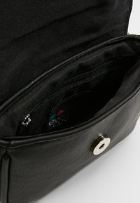 Sac à main synthétique noir à texture lisse, doté d'une poche intérieure zippée et d'une fermeture pression. Doublé en tissu noir.