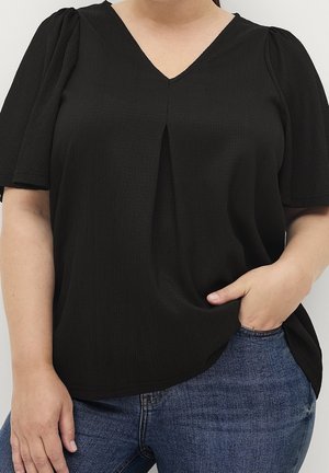 Sort V-hals top med korte pufærmer, med en plissering i midten, lavet af struktureret stof. Sættes sammen med blå denim jeans.