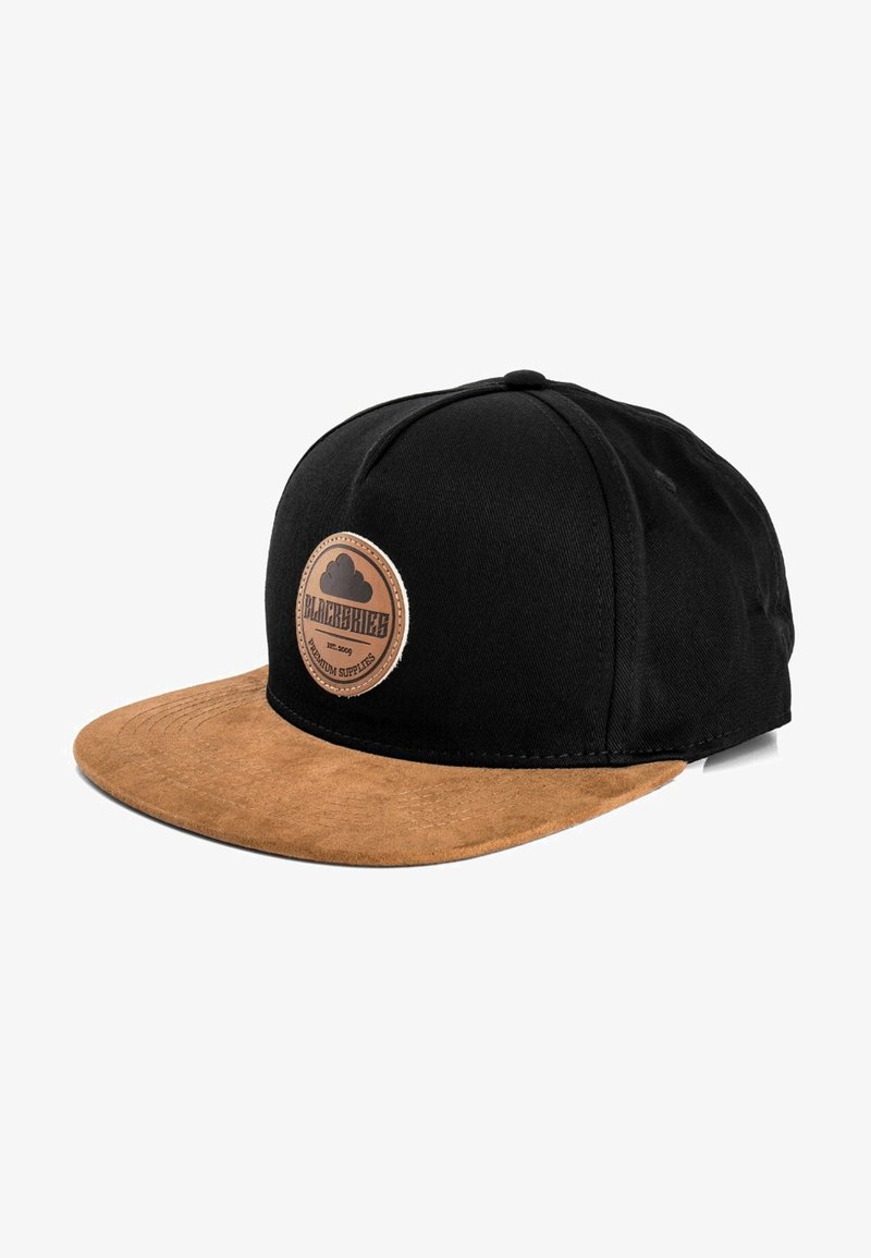 Black cap with a brown suede brim. Features a circular, embossed leather badge on the front. Cotton material, structured design.