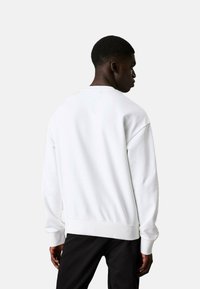 Sudadera blanca con puños y dobladillo acanalados, corte relajado y diseño minimalista. Tejido suave, cuello redondo y sin patrones visibles.