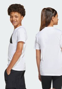 Weißes Baumwoll-T-Shirt mit einem schwarzen Grafikdesign auf der Vorderseite. Klassisches Rundhalsdesign, kurze Ärmel und entspannte Passform. Rückansicht sichtbar.