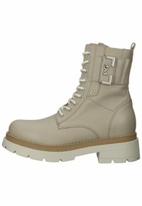Bota de tobillo de cuero beige con diseño de cordones, suela blanca gruesa en contraste y acento de logotipo metálico en el lateral. Parte superior texturizada y construcción robusta.
