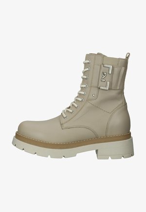 Beżowe skórzane botki za kostkę z wiązaniem, kontrastującą, masywną białą podeszwą i metalowym logo z boku. Teksturowana cholewka i solidna konstrukcja.