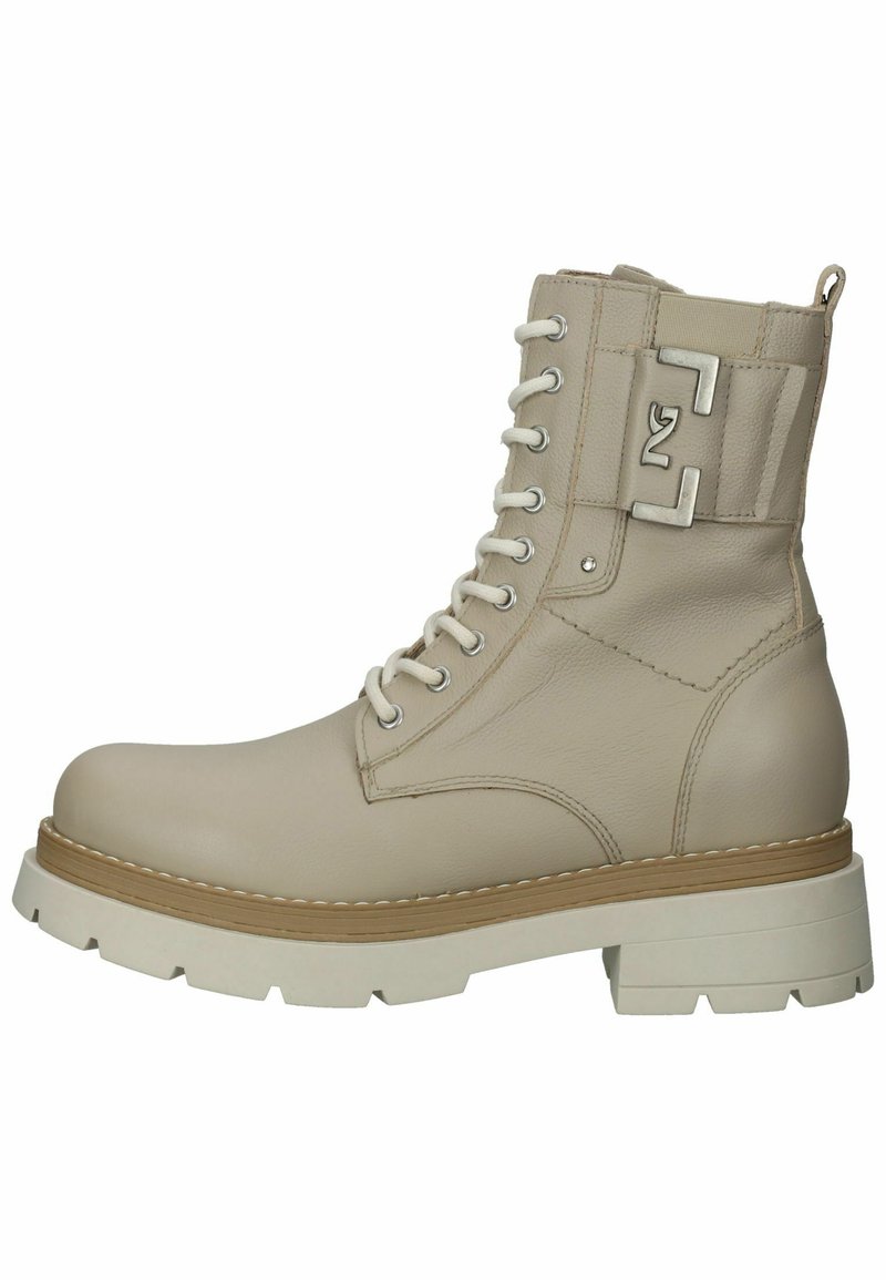 Bota de tobillo de cuero beige con diseño de cordones, suela blanca gruesa en contraste y acento de logotipo metálico en el lateral. Parte superior texturizada y construcción robusta.