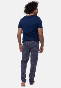 Mannen navy t-shirt gecombineerd met gestreepte pyjama broek in donkerblauw met rode en witte stippen, met een losse snit en zachte stof.