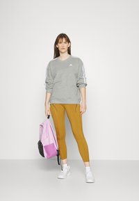 Sivý sweatshirt s bielymi pruhmi, horčicové legíny a ružovo-čierny batoh. Bílé športové topánky. Jednoduchý, priliehavý dizajn.