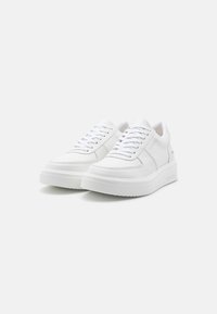 Zapatillas bajas blancas de cuero liso, con punta redonda, agujetas planas y una suela de plataforma que presenta una suela de goma texturizada.
