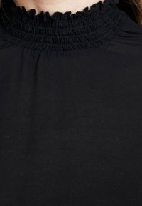 Blusa nera a collo alto con dettaglio di ruffle arricciato.