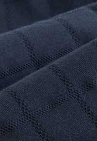 Temno modro pleteno blago z teksturiranim vzorcem prekrižanih linij, z mehkobo, gladko površino in dosledno tkanino po celotnem obsegu.