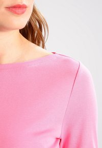 Rosa bomullströja med båtkrage och långa ärmar. Tyget är mjukt med en subtil ribbad textur.