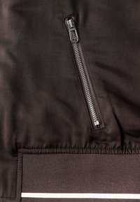 Gros plan sur un tissu sombre avec une fermeture éclair argentée verticale et un ourlet côtelé avec une bande horizontale blanche.