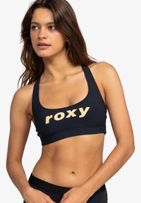 Navyblauwe sportbh met een breed bandontwerp, met een opvallend "roxy" logo in perzik. Gemaakt van een glad, elastisch materiaal.