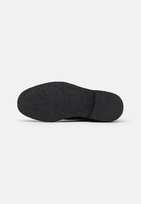 Suela negra de zapato con superficie de goma texturizada, punta redondeada y una cresta central. Diseñada para ofrecer agarre y durabilidad.