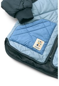 Μπεζέ μπουφάν σε μπλε και σκουροπράσινο ύφασμα, μ ε υφασμένη τσέπη και ετικέτα με το λογότυπο "LIEWOOD". Ζεστό, μονωμένο σχέδιο.