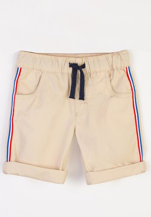 Shorts beiges avec revers, présentant des poches latérales et un cordon de serrage bleu marine. Des rayures rouges et bleues bordent les côtés. Matière en coton.