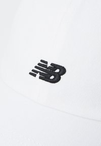 Hvit caps med buet skjerm og svart brodert "nb"-logo. Laget av teksturert stoff, med sømdetaljer langs kantene.