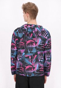 Jachetă cu glug�ă colorată, având un model geometric în roz, albastru și negru, cu palmieri și forme abstracte, realizată dintr-un material ușor.