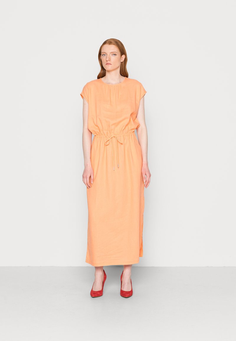 Vestido de linho laranja com mangas curtas e cintura ajustada. Apresenta uma silhueta solta e fendas laterais, combinado com sapatos de salto alto vermelhos.