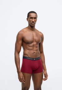 Rote Boxershorts mit kariertem Muster, aus weichem Stoff, mit einem marineblauen Bund und goldfarbener "TOMMY HILFIGER"-Beschriftung.