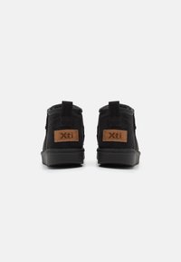 Botas de tobillo de ante negro con un acabado texturizado, que presentan detalles en cuero marrón y una tira en la parte trasera para facilitar su uso. Suelas gruesas.