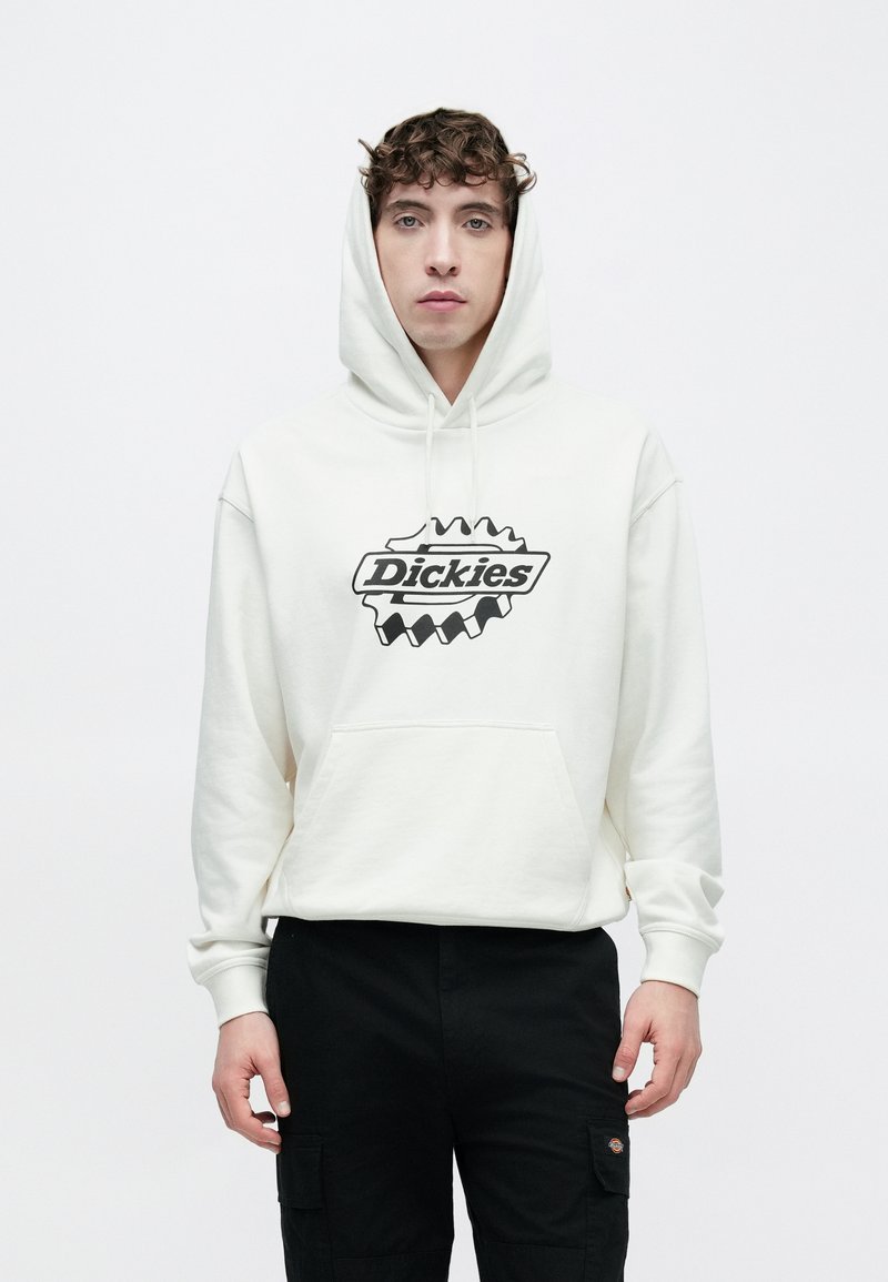 Felpa con cappuccio bianca con logo Dickies nero e una grande tasca a marsupio. Il modello la abbina a pantaloni cargo neri.