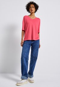 Růžová krátká rukávová verze s výstřihem do V, spárovaná s volně střiženými modrými džíny a bílými teniskami s béžovými akcenty. Jednoduchý design, příjemná textura.