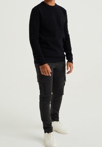 Tummansininen neulepaita, jossa on joustavat hihansuut ja helma, yhdistetty mustiin ruudullisiin cargo-housuihin ja valkoisiin lenkkareihin.