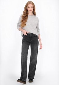 Grijze gebreide trui met een ontspannen pasvorm, gecombineerd met hoge taille, wijde zwarte jeans. Model draagt zwarte schoenen en toont een casual uitstraling.