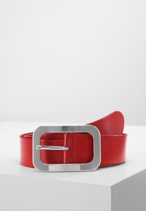 Rode leren riem met een grote rechthoekige zilverkleurige metalen gesp, geplaatst op een wit oppervlak tegen een effen achtergrond.