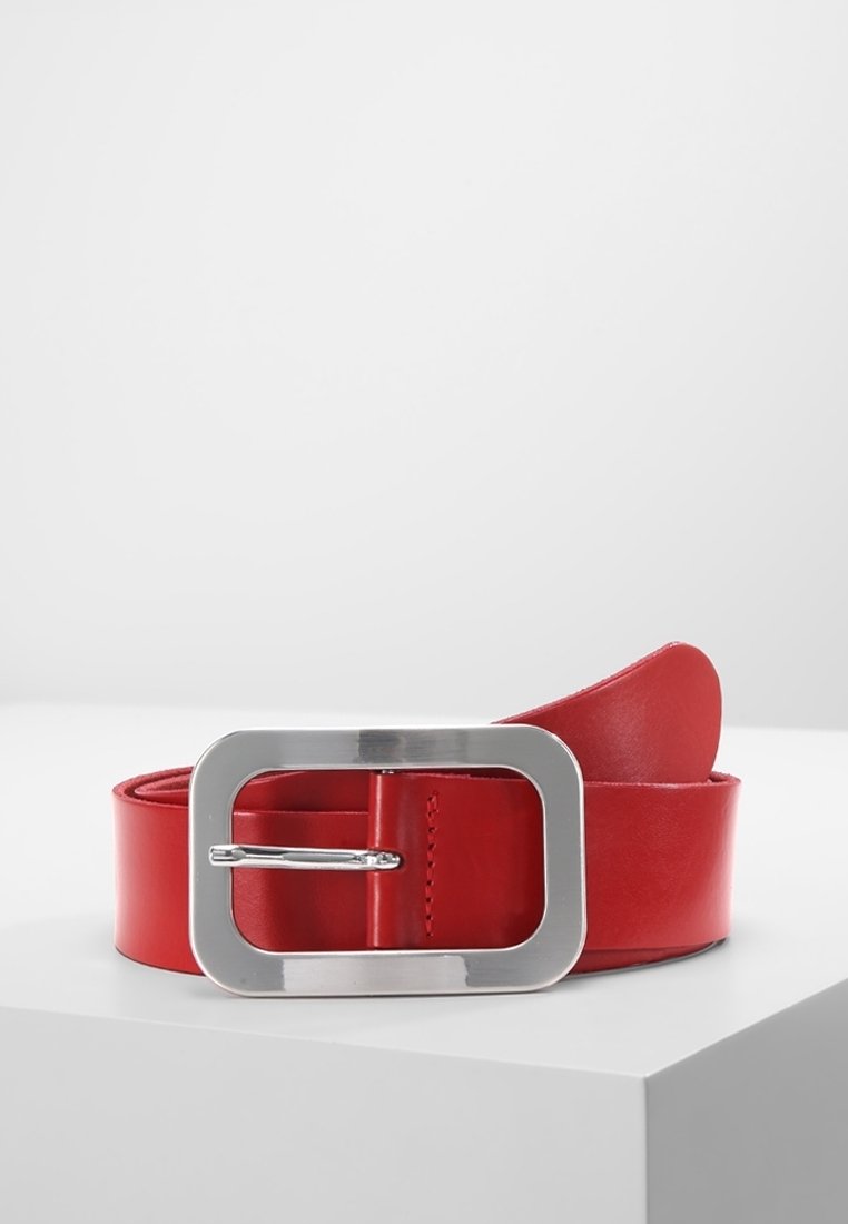 Ceinture en cuir rouge avec une grande boucle métallique argentée rectangulaire placée sur une surface blanche sur un fond uni.