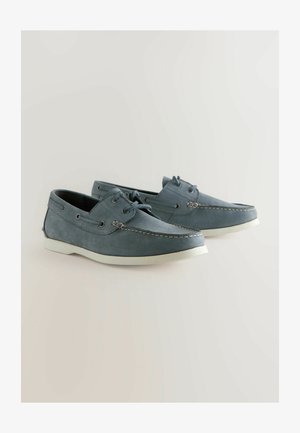 Kék bőr felsőrészű hajós cipők, fehér gumi talppal és kontrasztos varrással. Klasszikus fűzős dizájn fém fűzőlyukakkal.