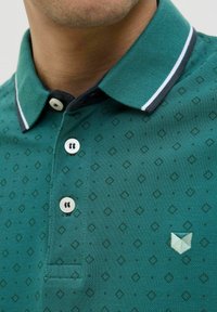 Tricou polo verde, realizat dintr-un material texturat cu un model în diamant. Are un guler cu dungi albe în contrast și două butoane.