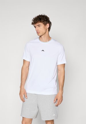 Hvid sports t-shirt med korte ærmer, rund hals og sort logo på brystet. Båret med grå shorts lavet af letvægtsmateriale.