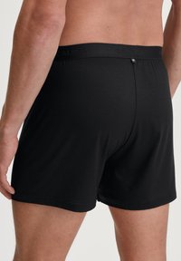 Zwarte katoenen boxershort met een gladde textuur en een elastische tailleband, met een merklogo en een eenvoudig, gestroomlijnd ontwerp.