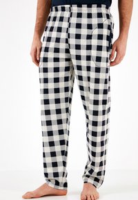Juosvos medvilninės pižamos kelnės juodai baltos languotos su laisvu siluetu, turi elastinę juosmenį ir šoninius kišenes. Visame paviršiuje matomas tekstūruotas plaid raštas.